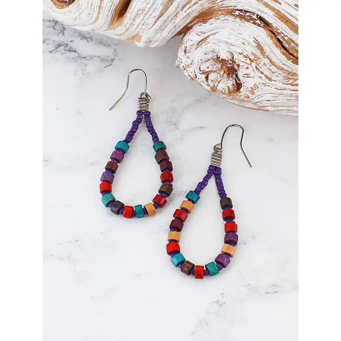 Colorful beaded earrings on a marble surface with seashells in the background