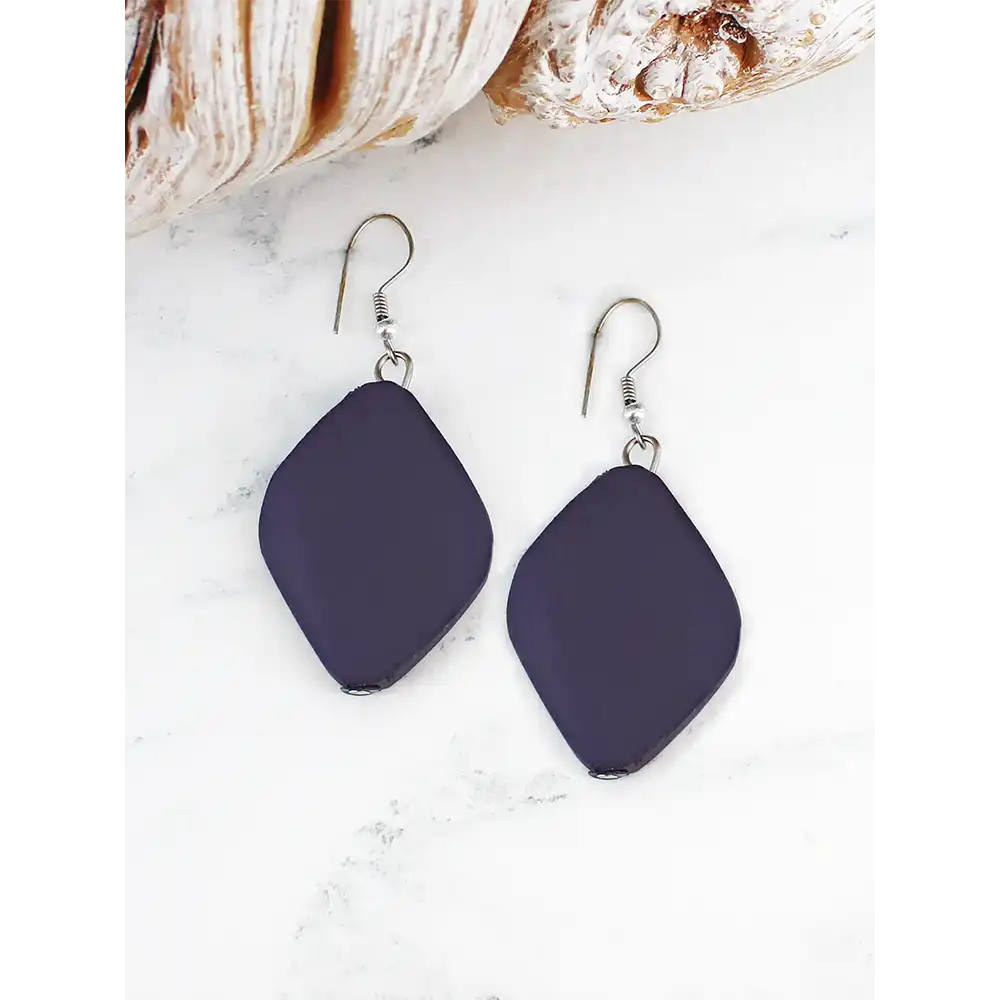 Navy blue earrings on a white surface with seashells in the background