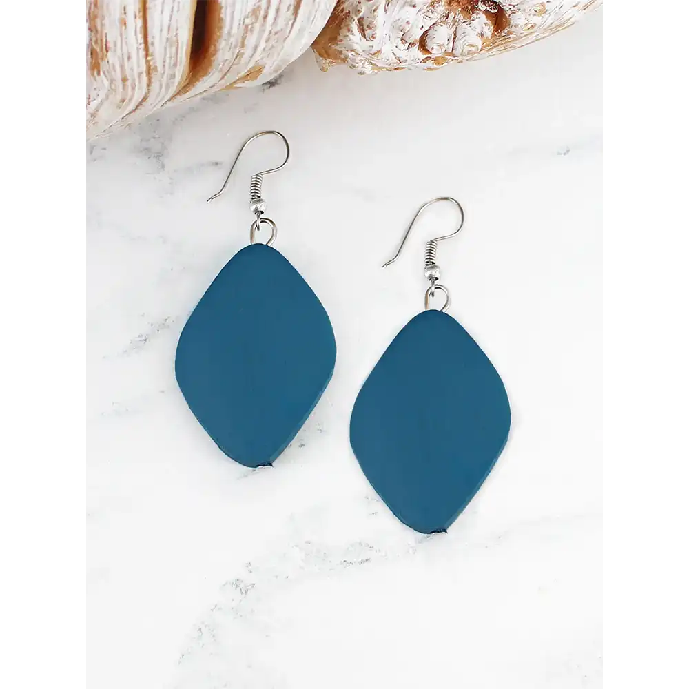 Blue earrings on a white marble surface with a shell and bread in the background
