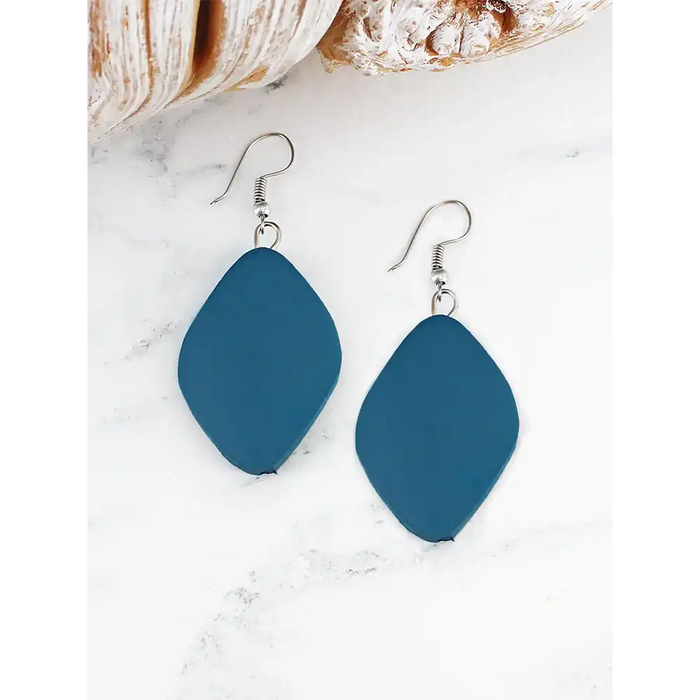 Blue earrings on a white marble surface with a shell and bread in the background