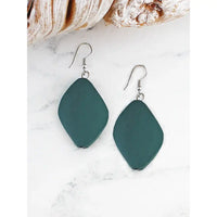 Teal earrings on a white marble surface with seashells in the background