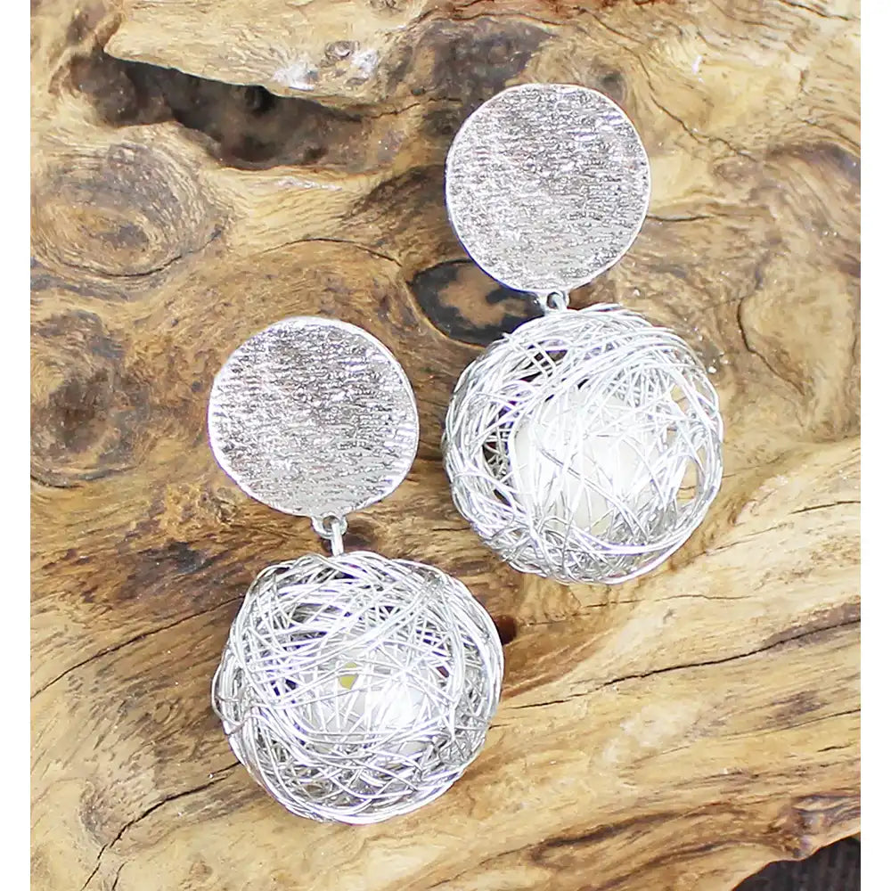 Silver earrings with textured circular designs on a wooden surface