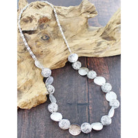 Silver beaded necklace on a wooden surface with natural light