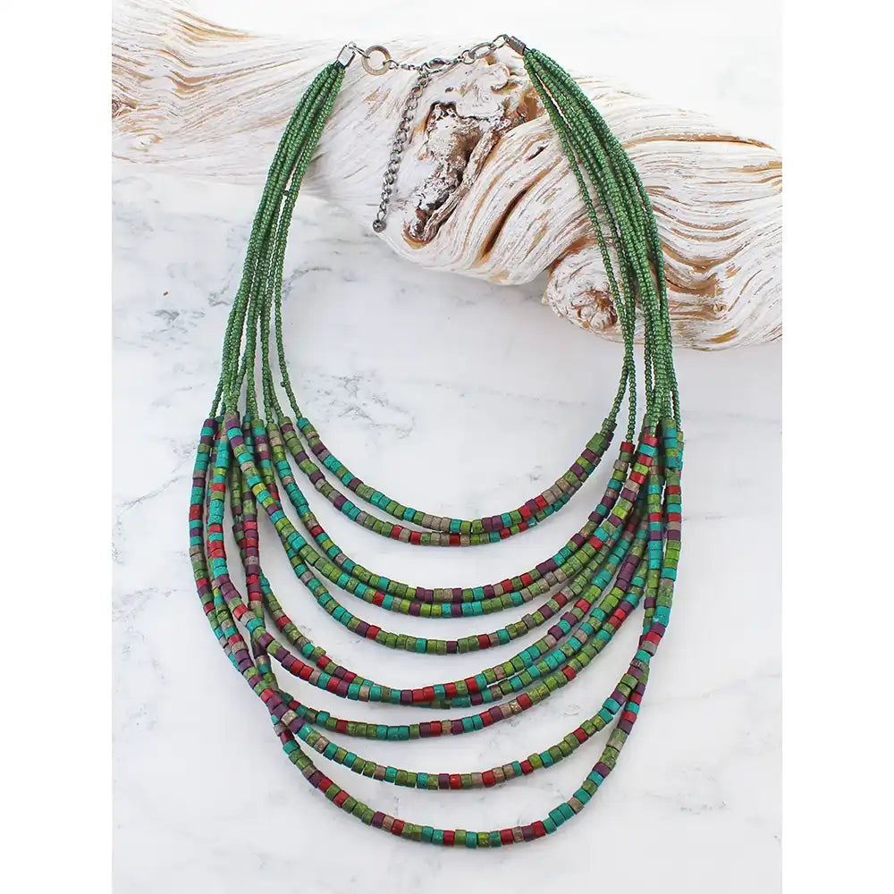 Multistrand beaded necklace with red and green hues on a white marble surface.