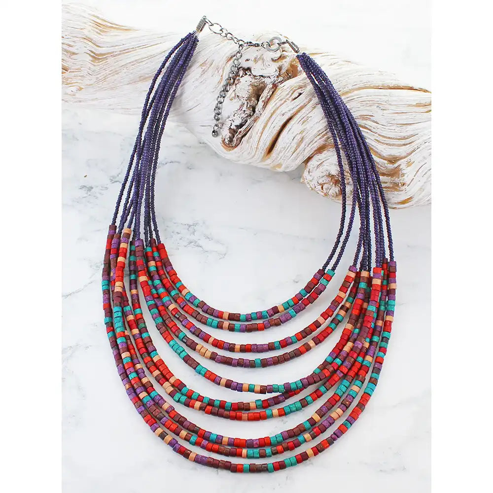 Colorful beaded necklace on a white surface with a shell in the background