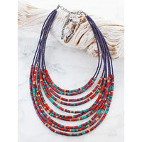 Colorful beaded necklace on a white surface with a shell in the background