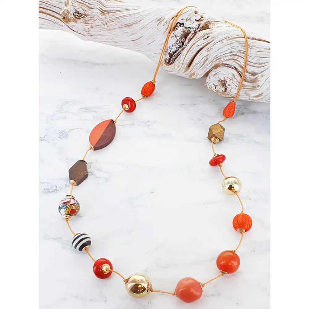 Long bead necklace with an assortment of different coloured and shaped beads on cord, resting on a piece of driftwood.