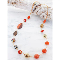 Long bead necklace with an assortment of different coloured and shaped beads on cord, resting on a piece of driftwood.
