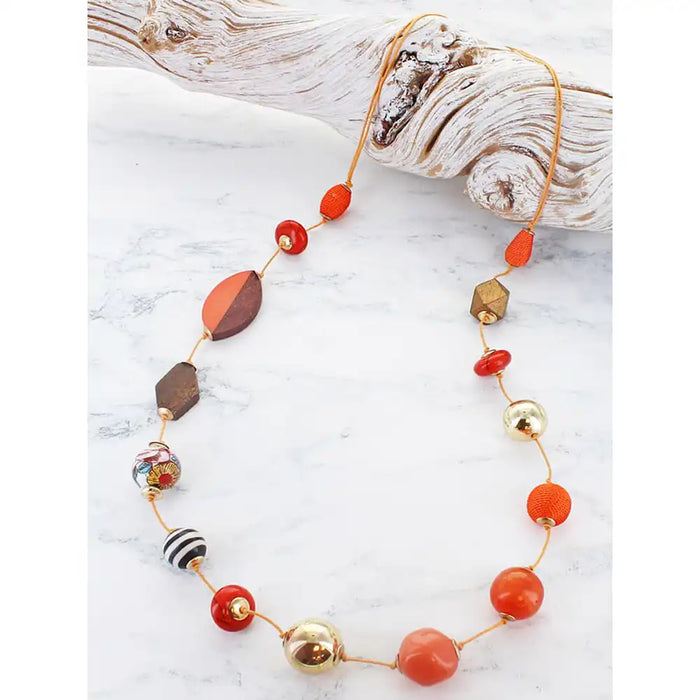 Long bead necklace with an assortment of different coloured and shaped beads on cord, resting on a piece of driftwood.