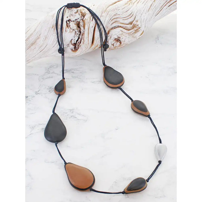 Long necklace with resin black and brown beads on black cord, resting on driftwood.