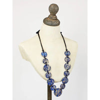 A long statement necklace with round blue and gol beads on a black cord, displayed on a cream-colored mannequin bust.