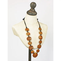 A long statement necklace with large, round, textured amber-brown beads on a black cord, displayed on a cream-colored mannequin bust.