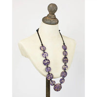 A long beaded necklace with oval purple and white marbled beads on a black cord, displayed on an off-white mannequin bust against a light gray background.