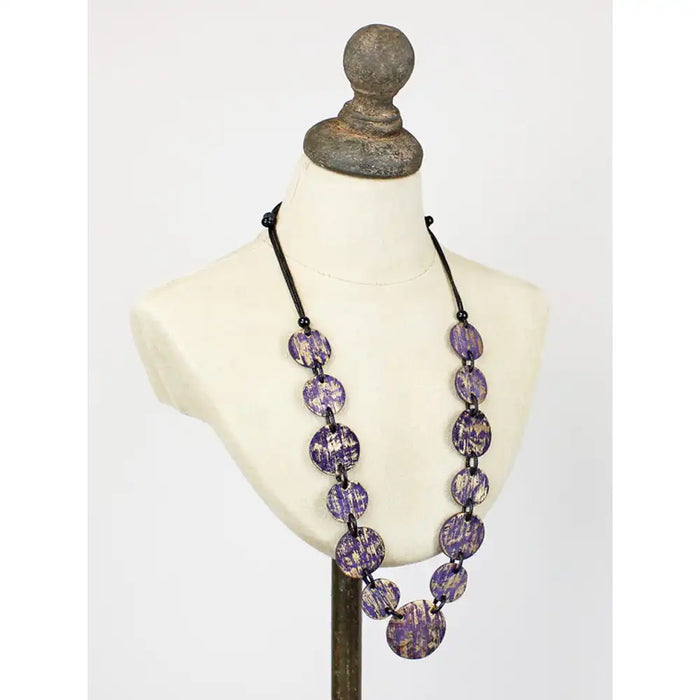 A long beaded necklace with oval purple and white marbled beads on a black cord, displayed on an off-white mannequin bust against a light gray background.