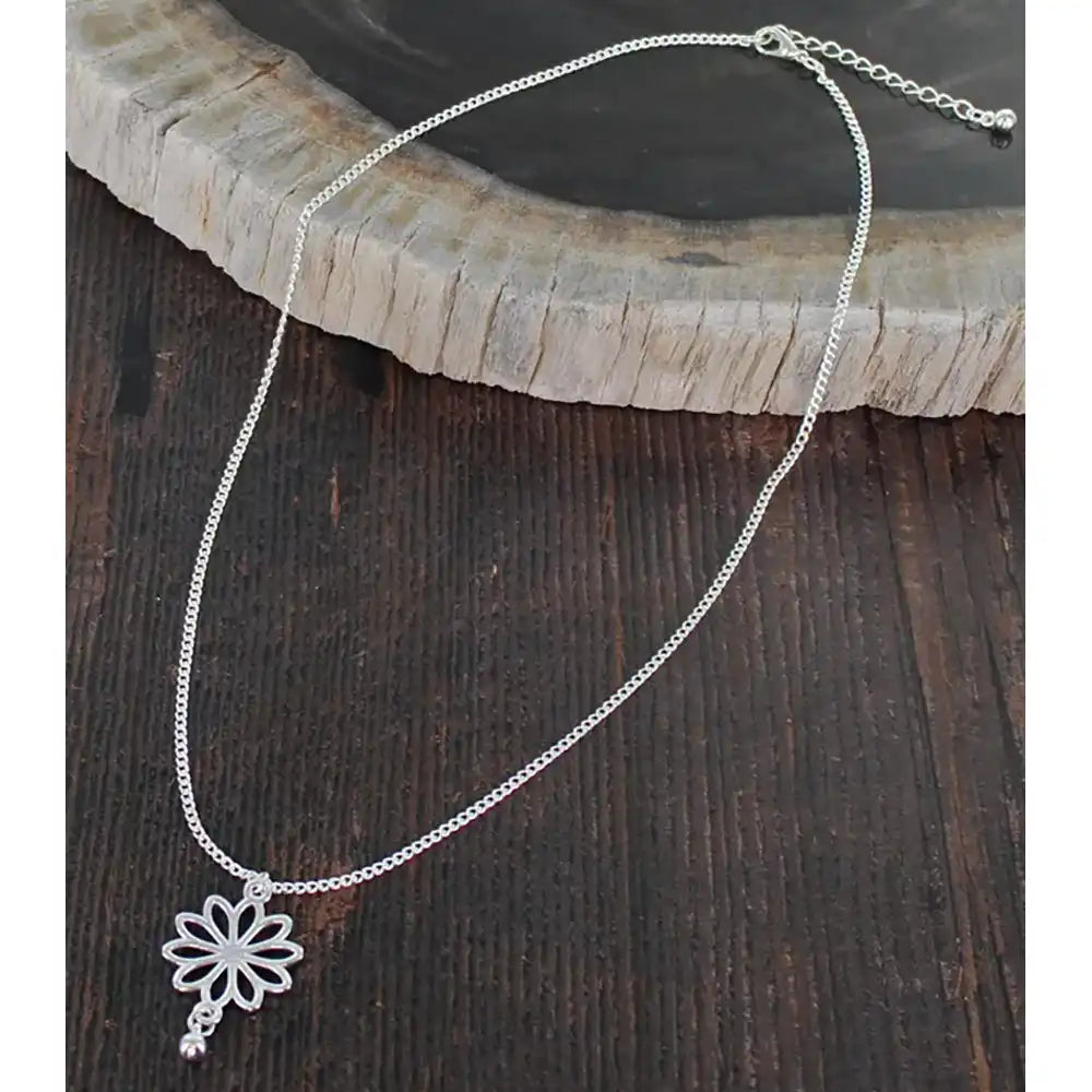 Silver necklace with a flower pendant on a wooden surface