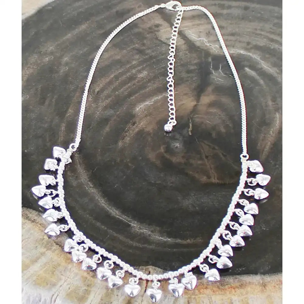 Silver necklace with heart-shaped pendants on a wooden surface