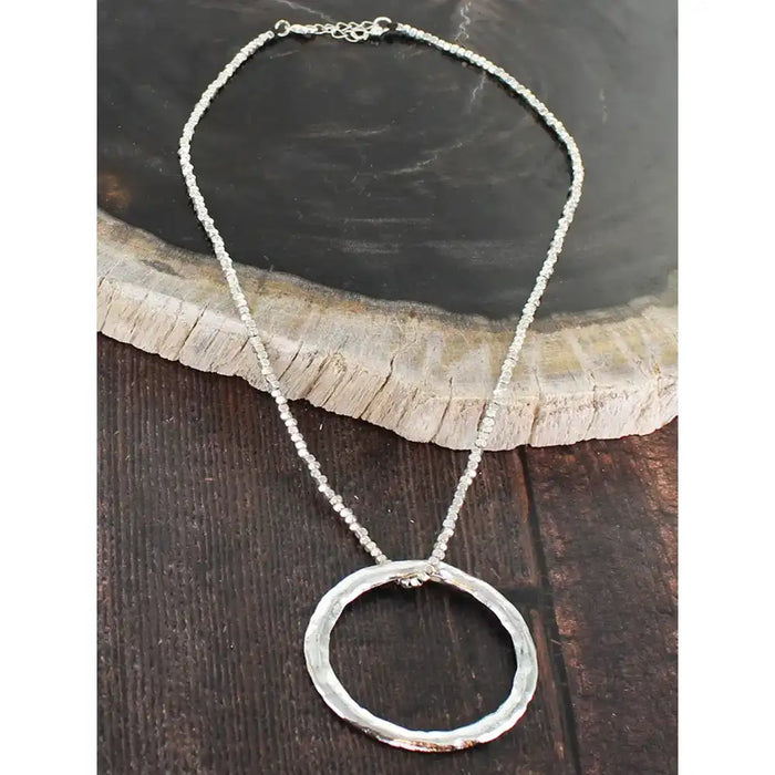 Silver necklace with a circular pendant on a wooden surface