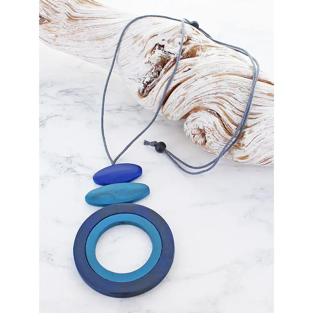 Blue necklace with layered pendants on a white surface with driftwood.