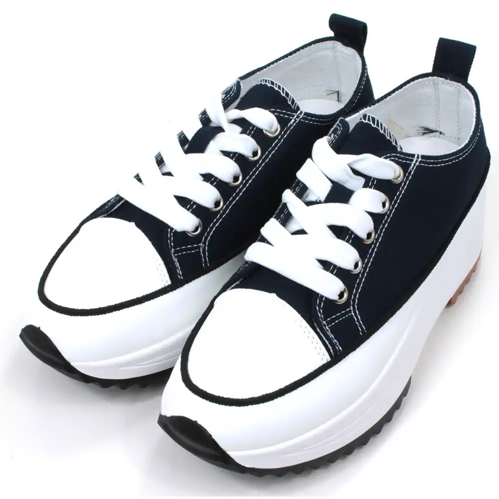 Lace up platform trainers in navy blue. White trim around the base above the black soles. White toe caps. Fabric shoe bodies. Navy blue pull on tabs at the ankles. White stitching detail. Angled view.