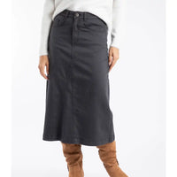 Person wearing a black skirt with a white top and brown boots on a white background