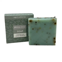 A handmade soap bar with dark specks next to its packaging box. The box is sage green with a leaf pattern and reads 'sage & white tea' and 'Wild-Olive SOAP'.