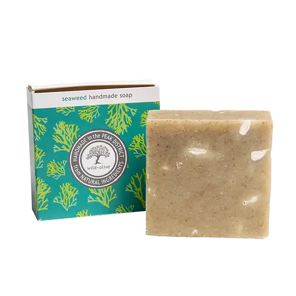A rectangular bar of handmade seaweed soap in a speckled beige tone, shown next to its teal and white retail box with green seaweed illustrations. The box reads 'seaweed handmade soap'.
