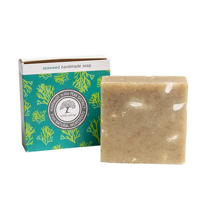 A rectangular bar of handmade seaweed soap in a speckled beige tone, shown next to its teal and white retail box with green seaweed illustrations. The box reads 'seaweed handmade soap'.