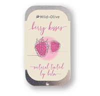 Wild-Olive Berry Kisses natural tinted lip balm in a silver metal tin with a cream-colored label featuring pink raspberry illustrations and pink script text.