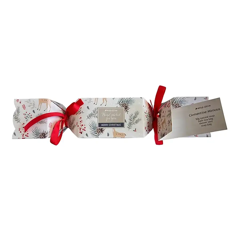 A Christmas-themed gift cracker package wrapped in white paper with a festive print of deer, pinecones, mistletoe, and red berries, tied with red ribbons and accompanied by a small paper tag detailing contents of the cracker.