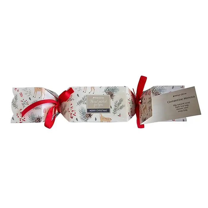 A Christmas-themed gift cracker package wrapped in white paper with a festive print of deer, pinecones, mistletoe, and red berries, tied with red ribbons and accompanied by a small paper tag detailing contents of the cracker.