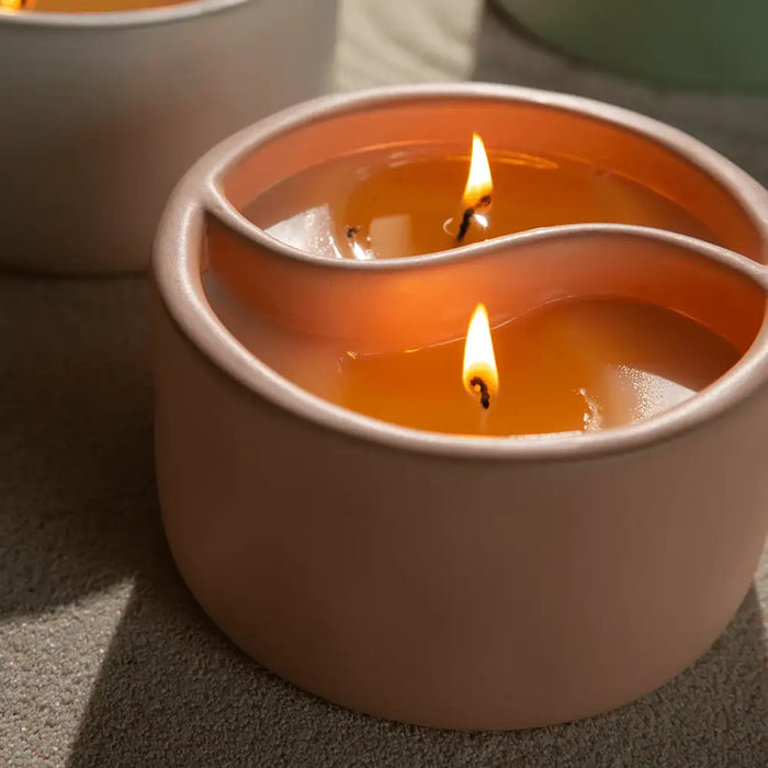 Candle in a wavy container with flames on a neutral background