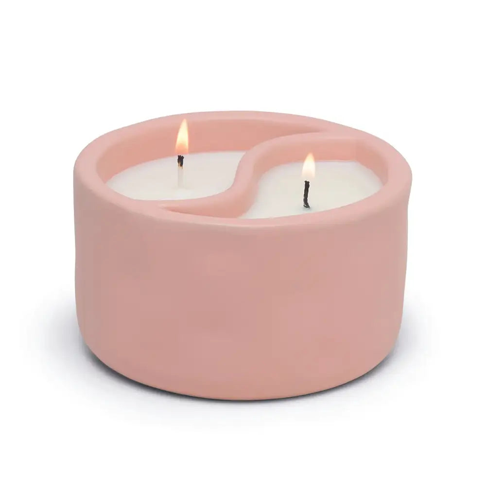 Pink ceramic candle holder with two lit candles on a white background