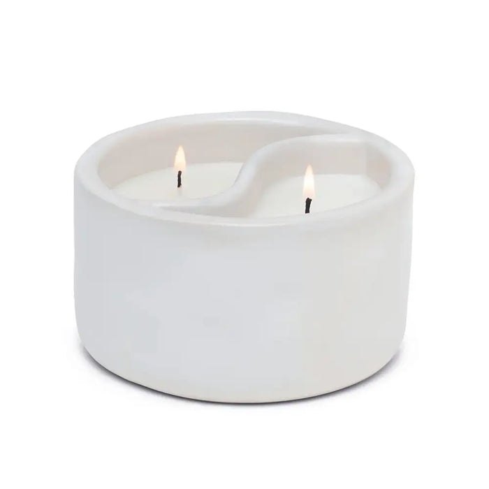 White ceramic candle holder with two lit candles on a white background