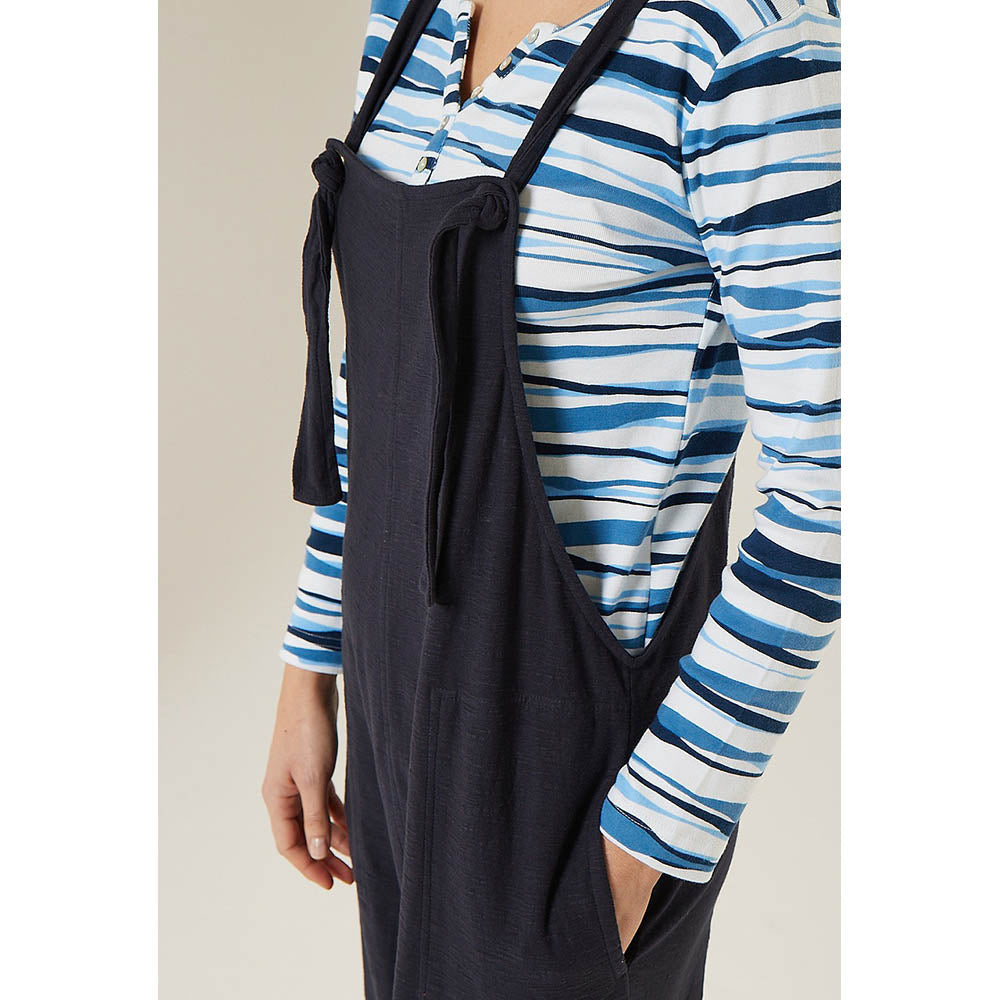 Adini Lucie dugarees in navy blue. Side pockets. Bib is fastened with knots in the straps. Leg length is on the ankle with turn ups. View showing close up of strap to bib fitting.