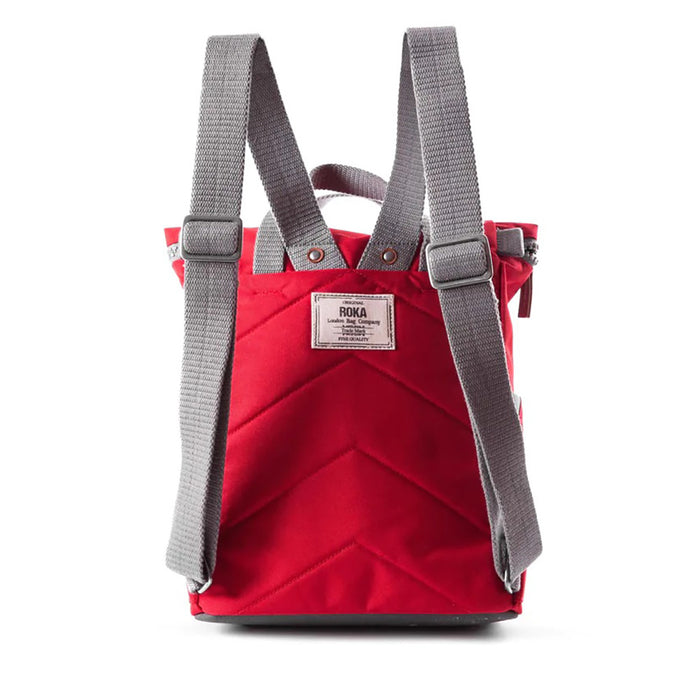 Roka red backpack. Foldover and zip fastening at the top. External zip fastening pocket. Grey handles and back pack straps. Two water bottle pockets. Rear view showing padding and Roka label.