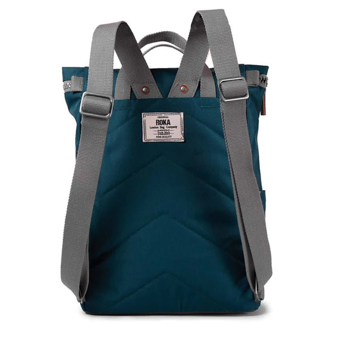 Roka teal backpack. Foldover and zip fastening at the top. External zip fastening pocket. Grey handles and back pack straps. Two water bottle pockets. Rear view showing padding and Roka label.
