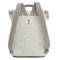 Roka light grey backpack. Foldover and zip fastening at the top. External zip fastening pocket. Grey handles and back pack straps. Two water bottle pockets. Rear view showing padding and Roka label.