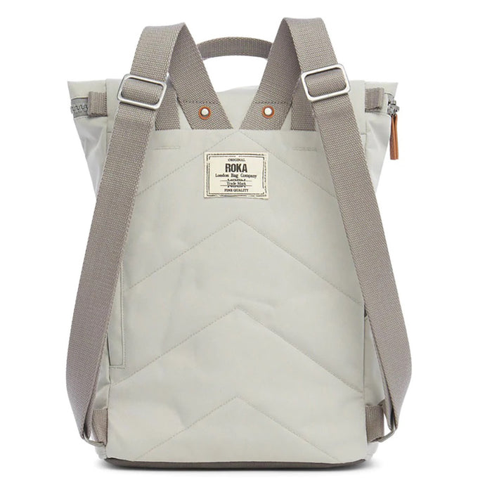 Roka light grey backpack. Foldover and zip fastening at the top. External zip fastening pocket. Grey handles and back pack straps. Two water bottle pockets. Rear view showing padding and Roka label.